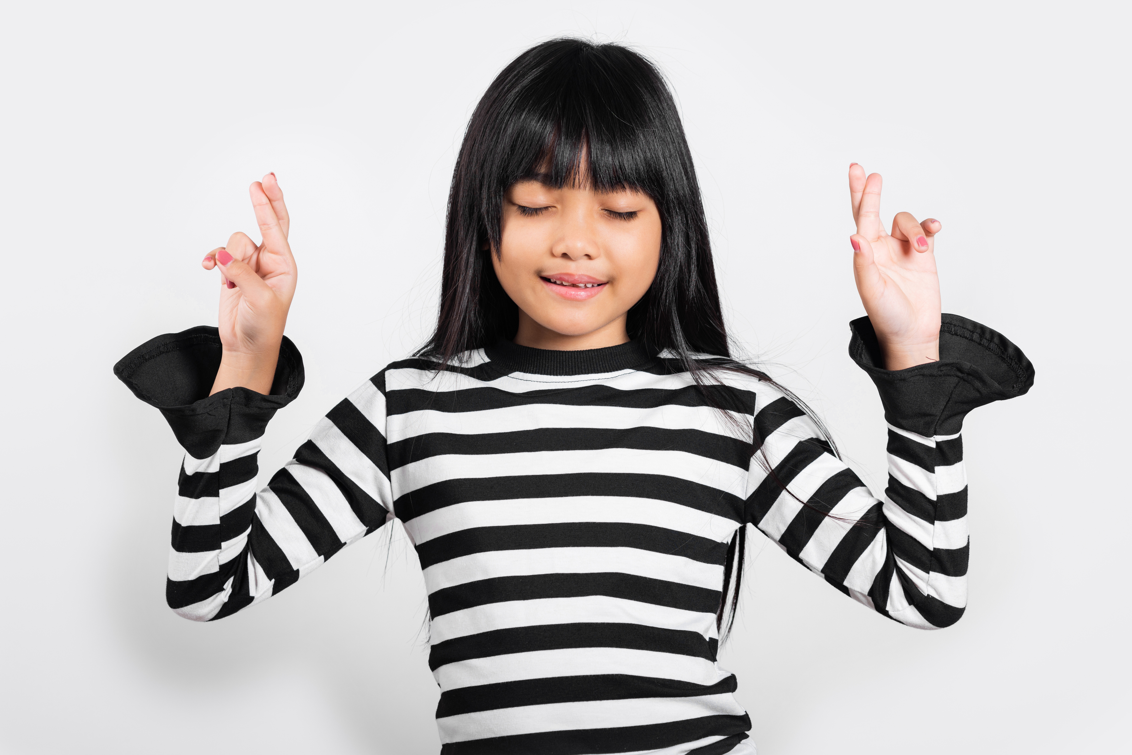 A girl with her eyes closed and both hands raised, making peace signs with her fingers while smiling gently